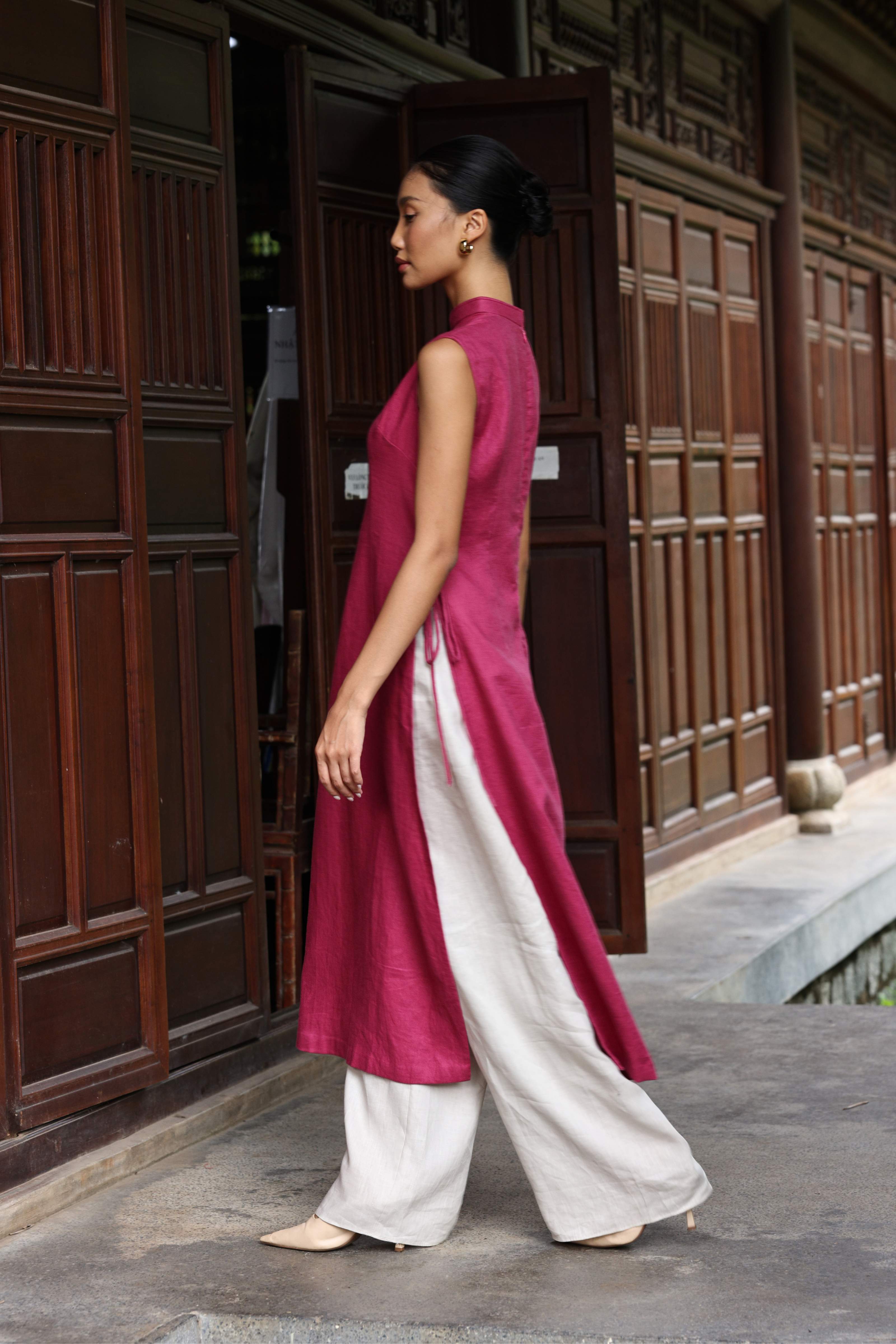 Woman in a pink and white traditional outfit standing in front of wooden doors.