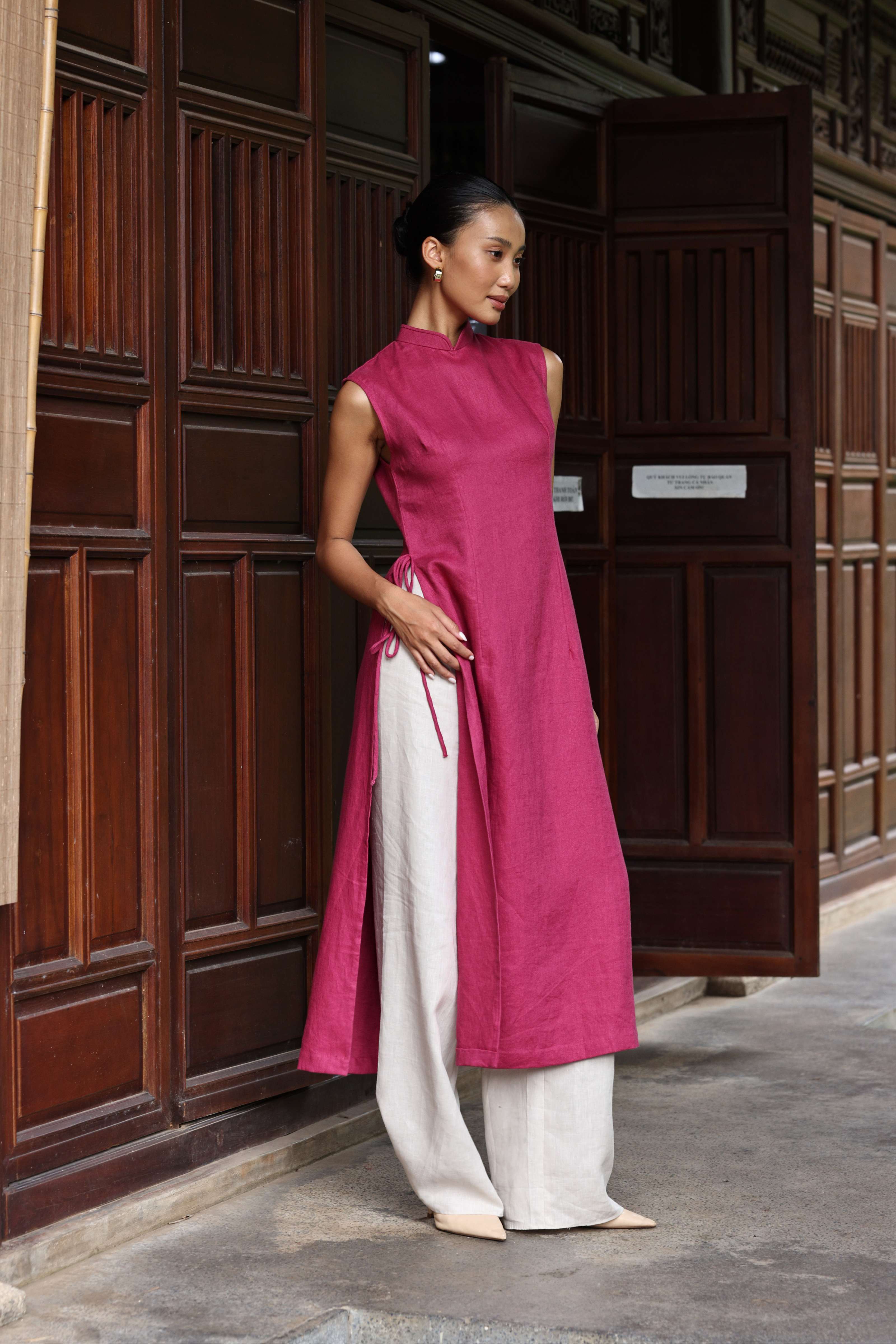Woman wearing a pink and white traditional outfit standing in front of a wooden door.