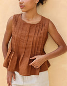 Woman wearing a brown sleeveless top against a beige background