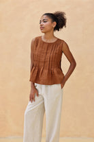 Woman wearing a brown sleeveless top and pants against a beige background