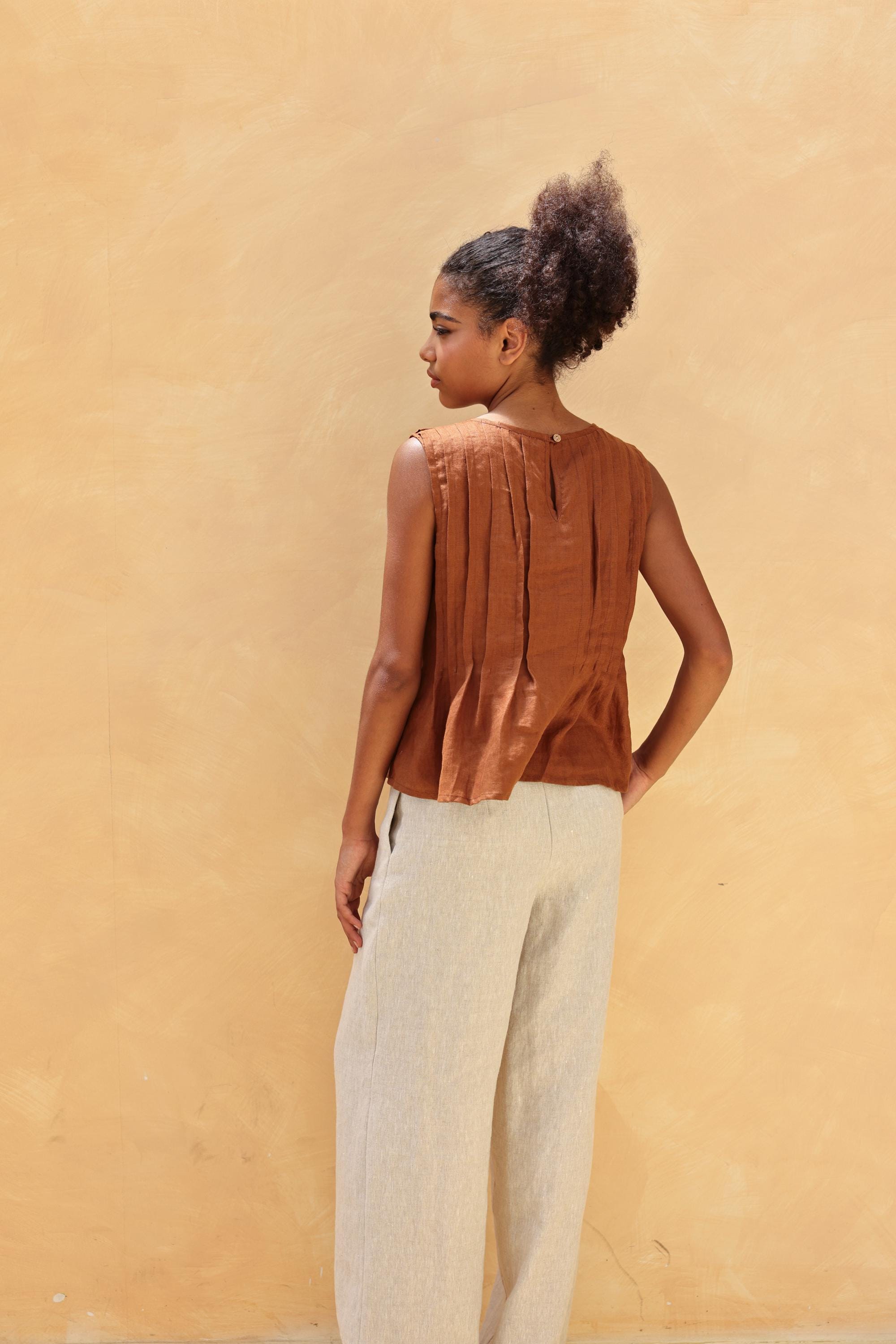 Woman wearing a brown sleeveless top and beige pants against a yellow wall