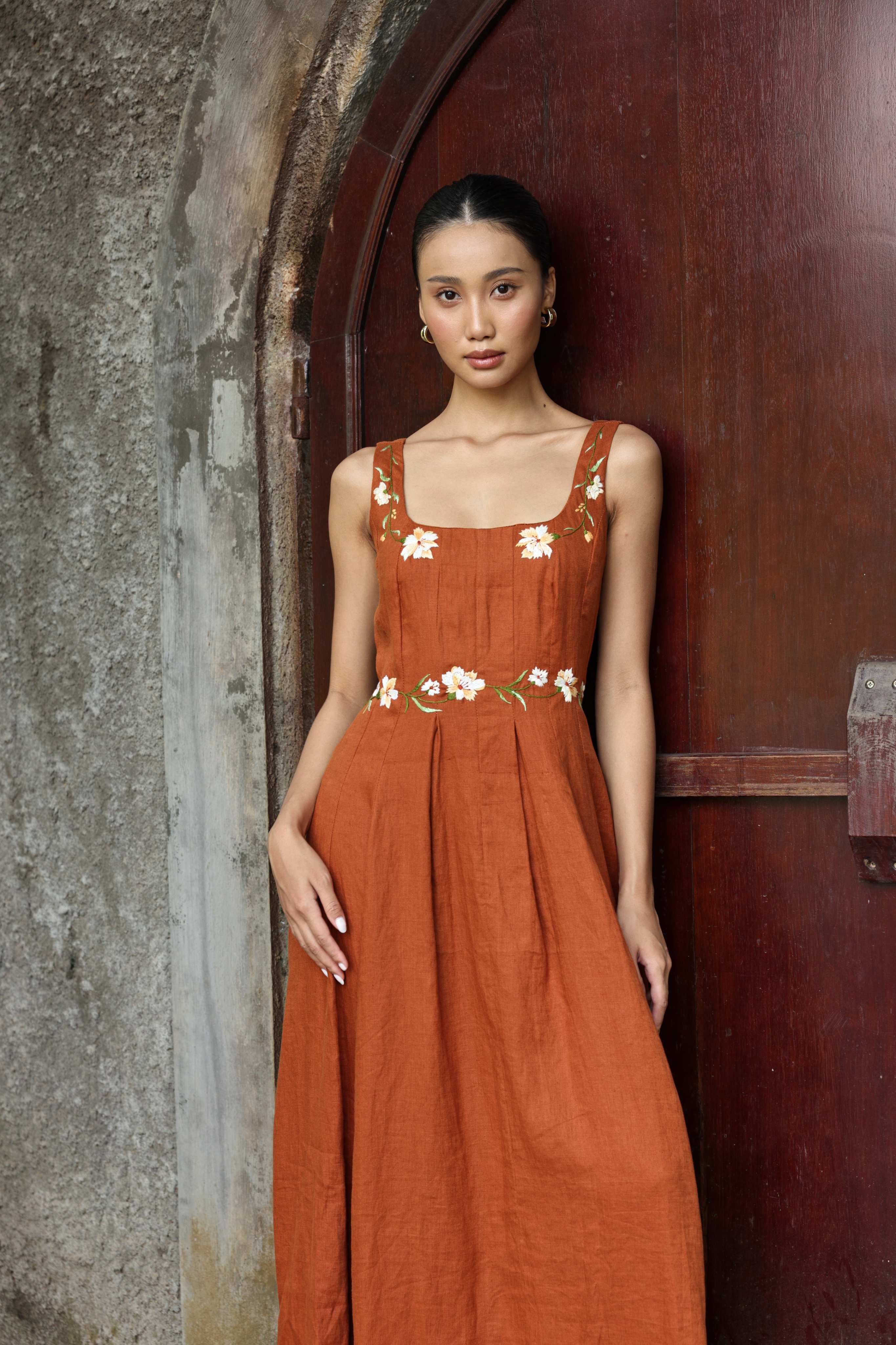 Woman wearing a floral dress standing against a textured wall.