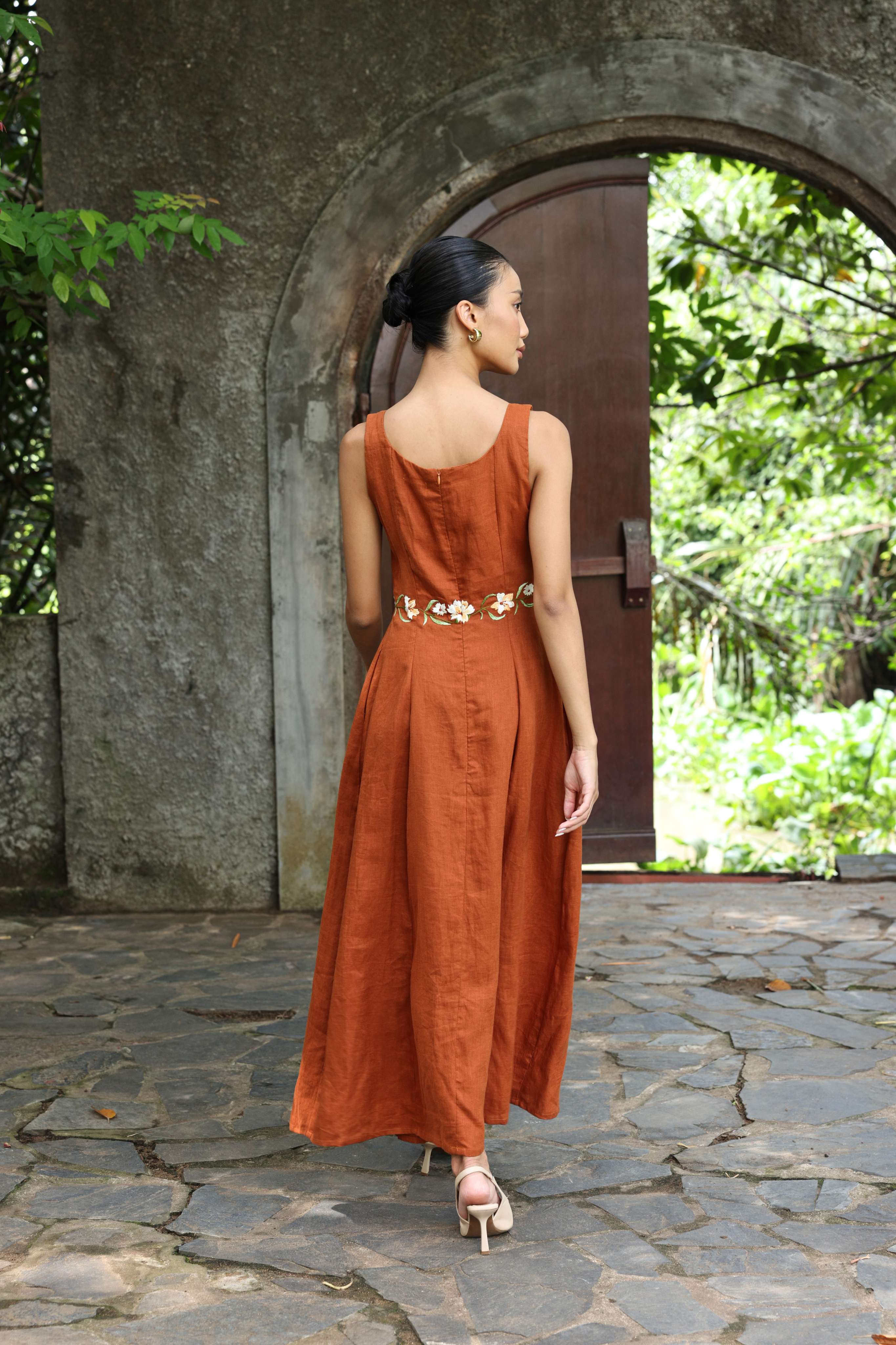 Woman in a rust-colored dress standing in front of a stone archway with greenery.