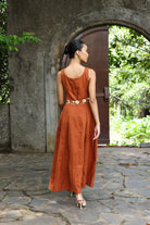 Woman in a rust-colored dress standing in front of a stone archway with greenery.