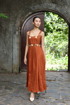 Woman in a rust-colored dress standing in front of an archway with greenery.