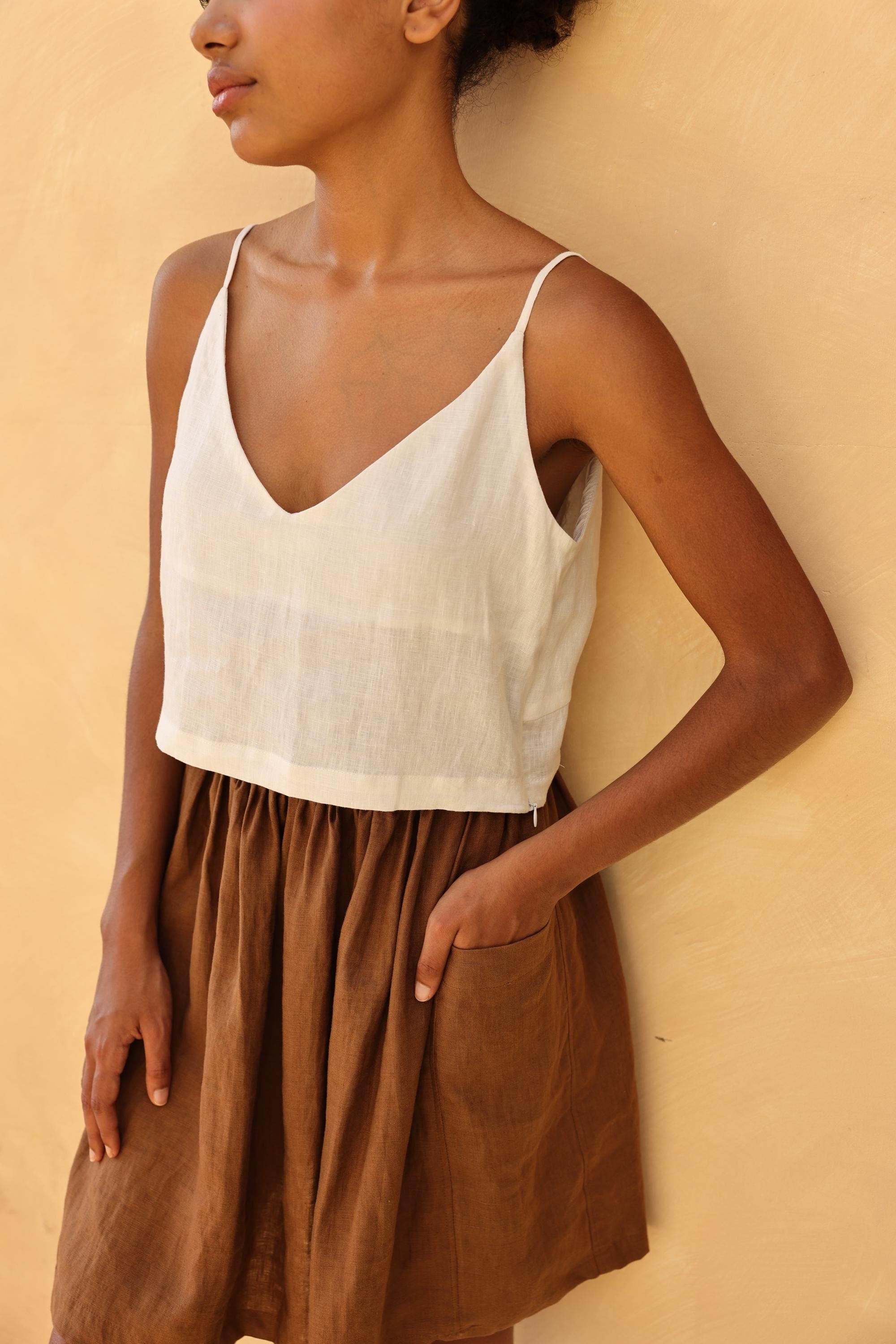 Person wearing a white top and brown skirt against a beige wall