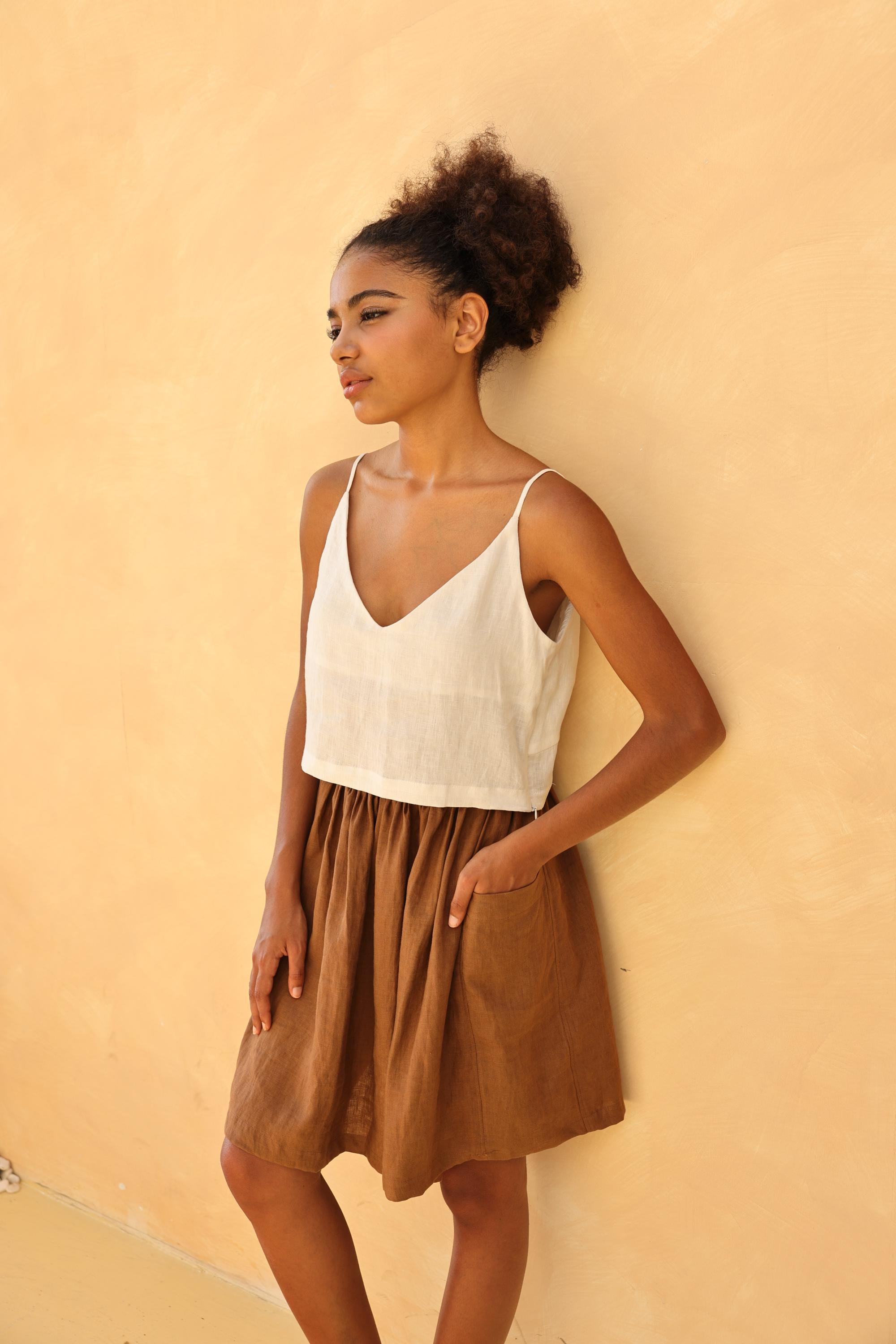 Woman wearing a white top and brown skirt against a beige wall