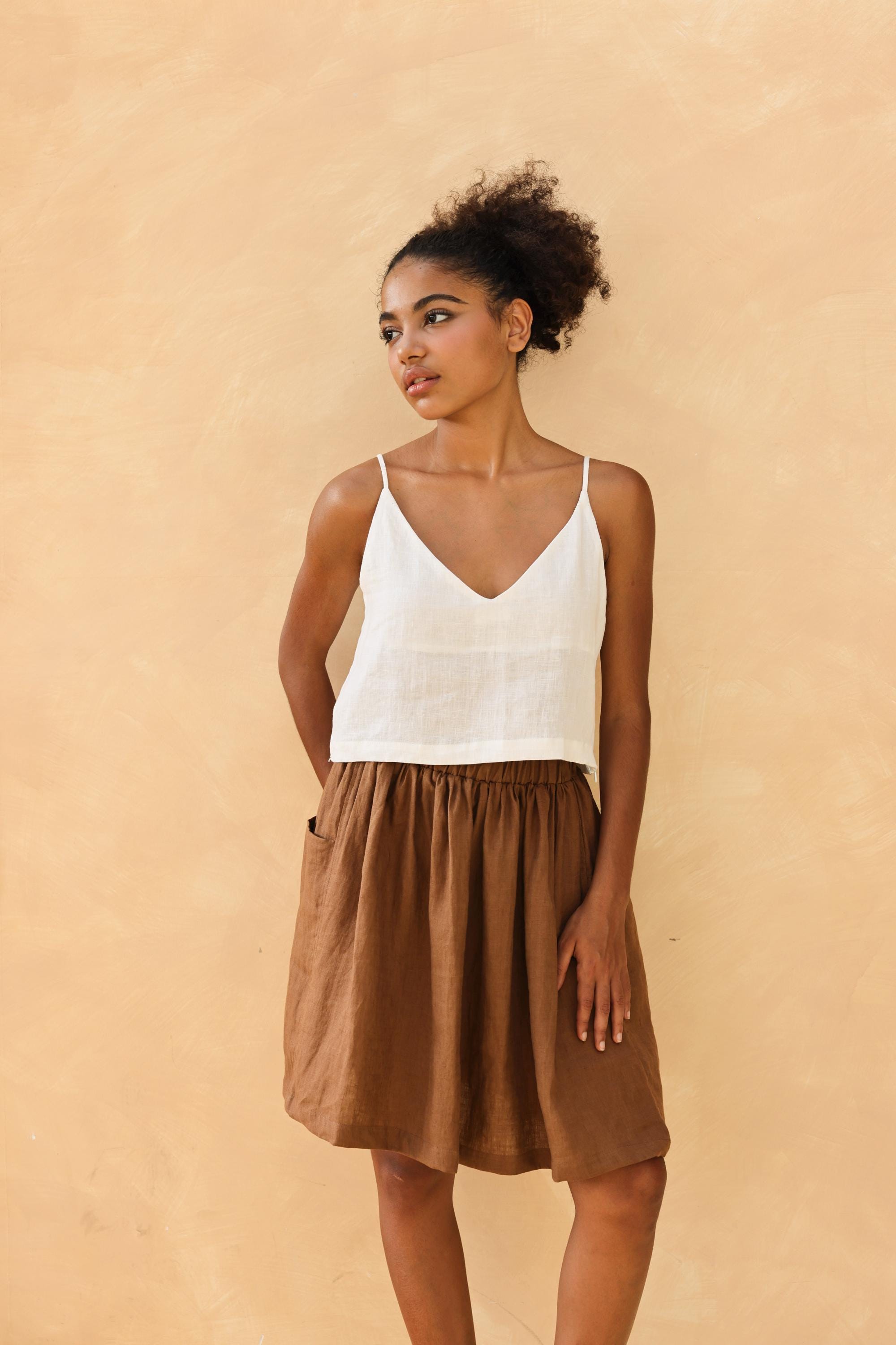 Woman wearing a white top and brown skirt against a beige background