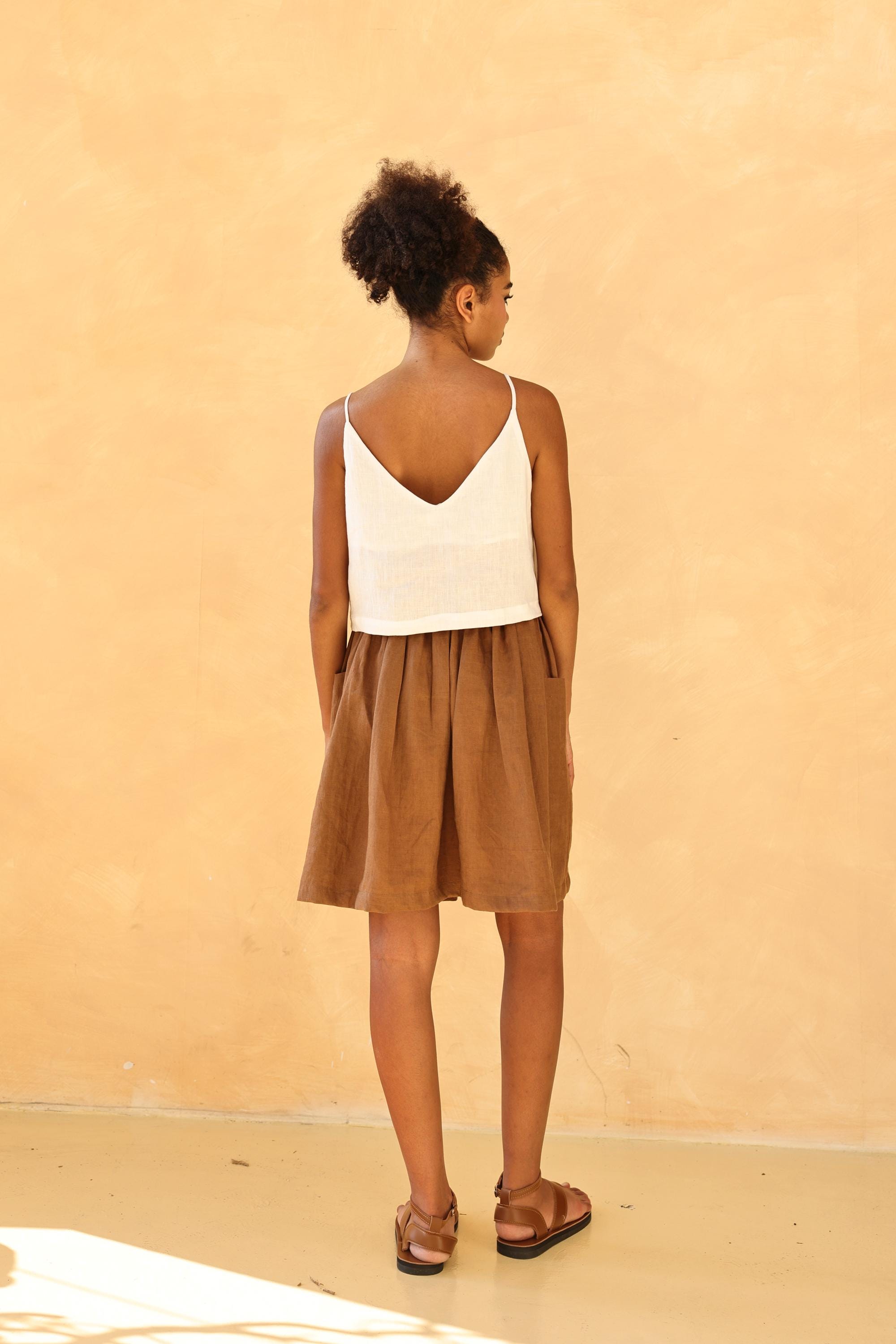 Woman wearing a white top and brown skirt against a beige background