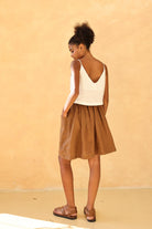 Woman wearing a white top and brown skirt against a beige background