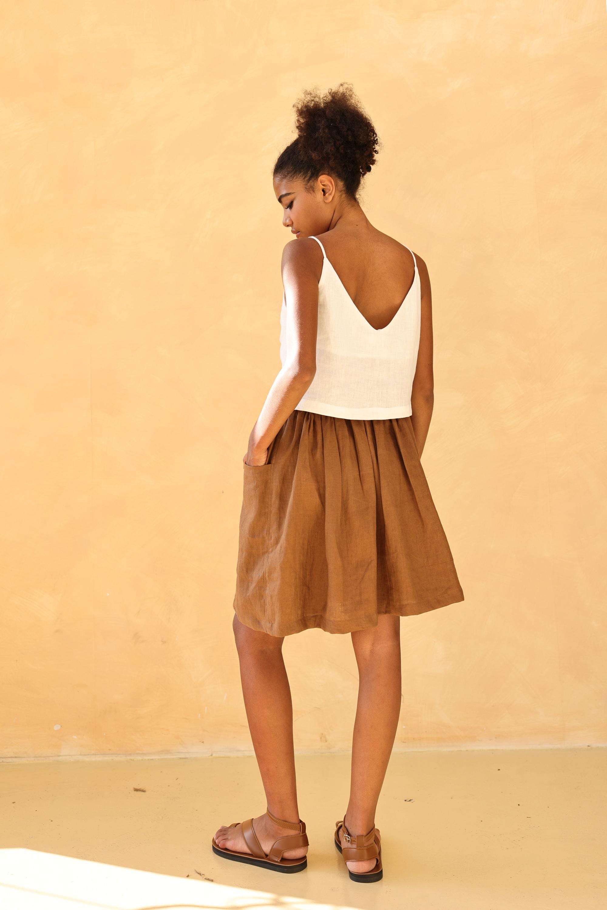 Woman wearing a white top and brown skirt against a beige background