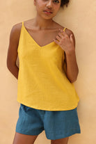 Woman wearing a yellow top and blue shorts against a beige background
