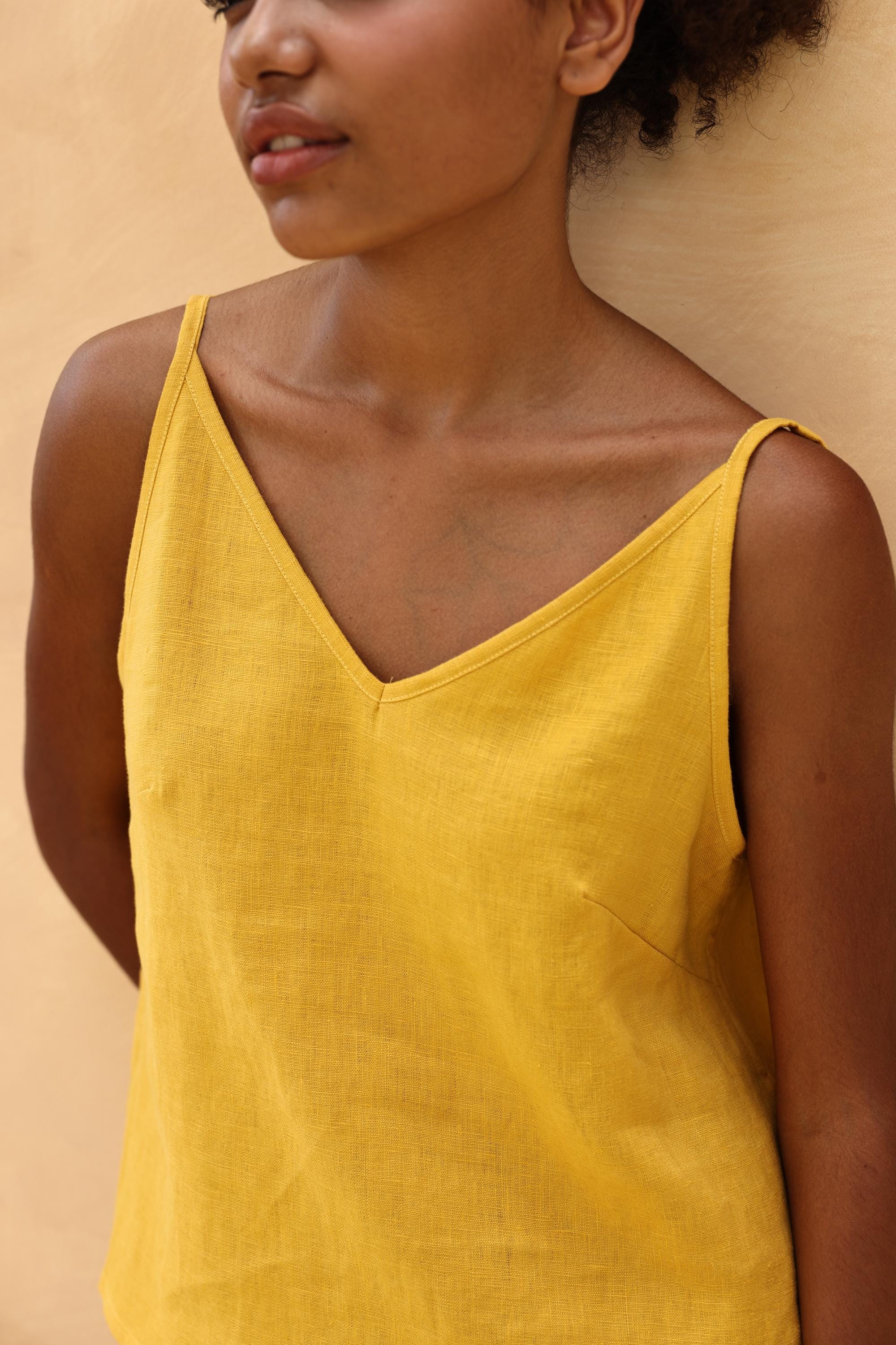 Woman wearing a yellow sleeveless top against a beige background