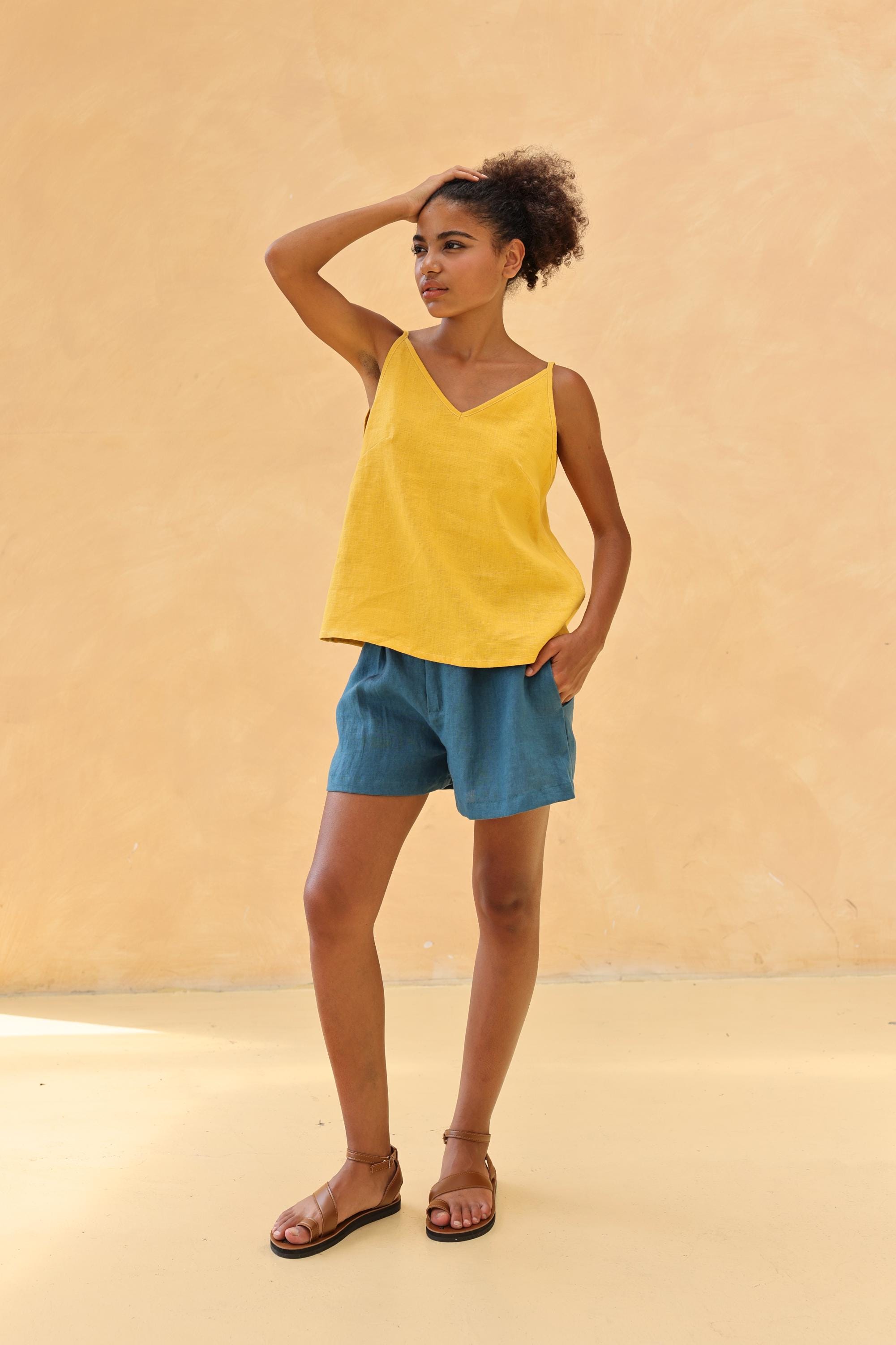 Woman wearing a yellow top and blue shorts against a beige background