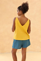 Woman wearing a yellow sleeveless top and blue shorts against a beige background