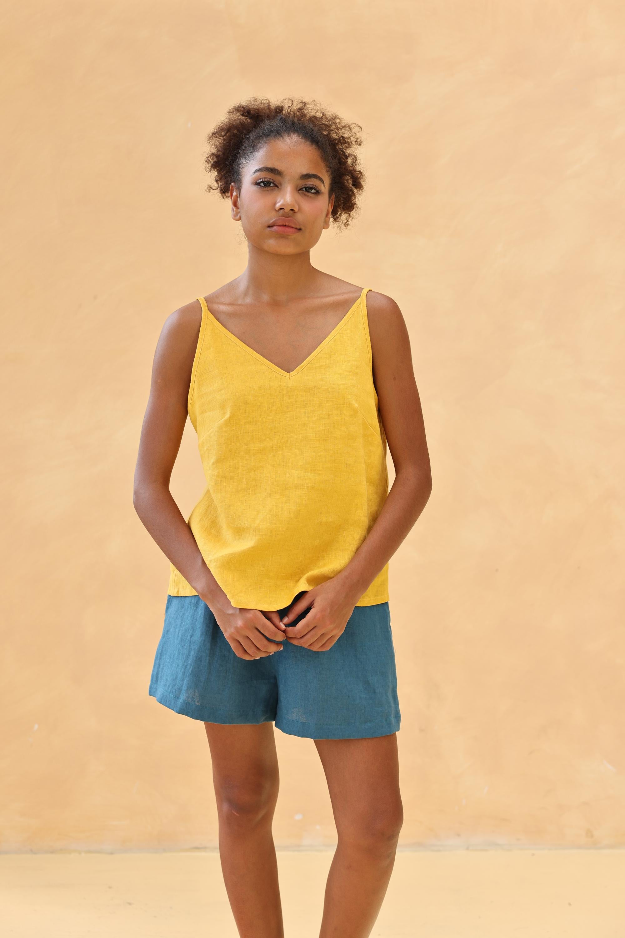 Woman wearing a yellow tank top and blue shorts against a beige background