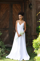 Woman in a white wedding dress holding flowers in front of wooden doors.