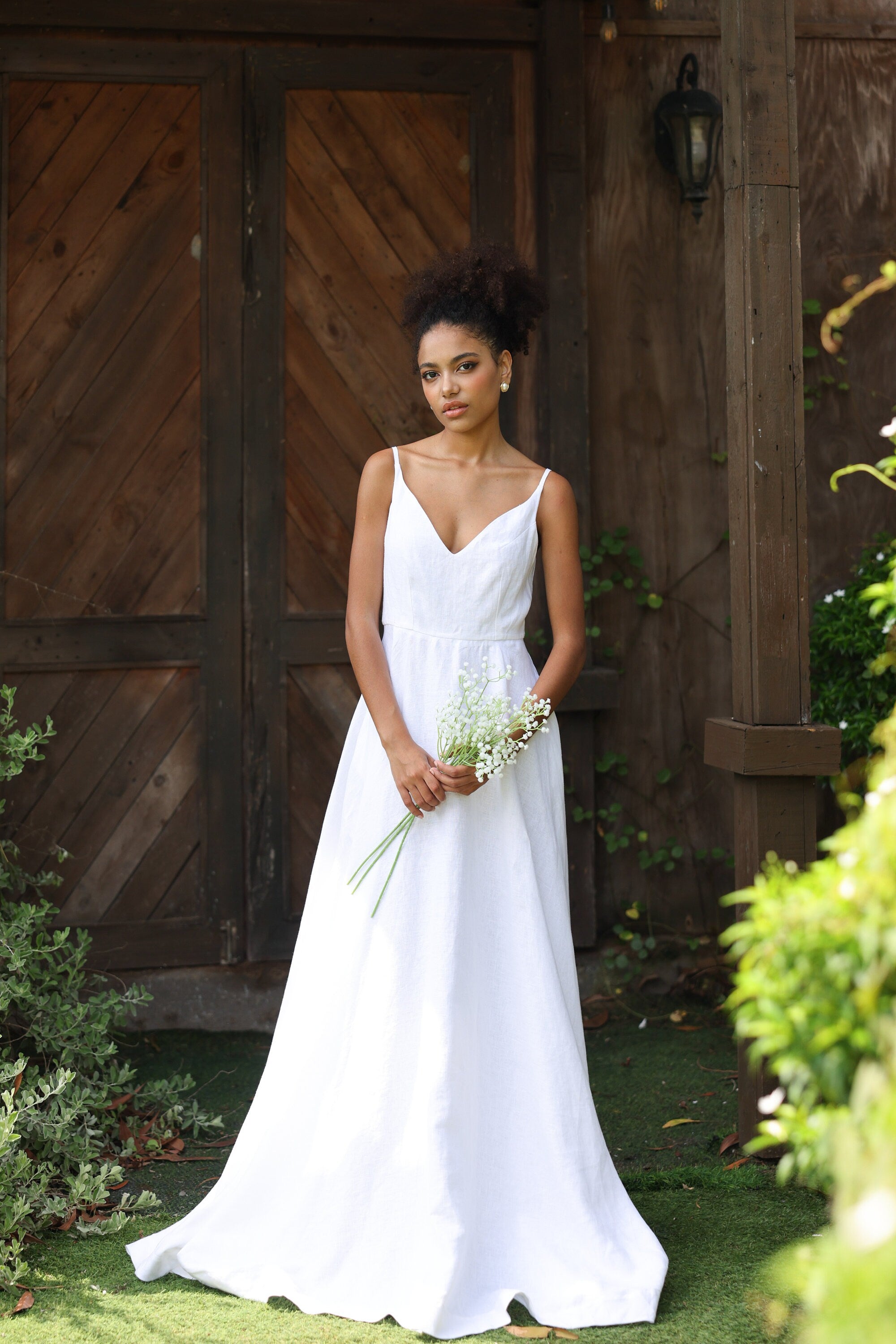Woman in a white wedding dress holding flowers in front of wooden doors.