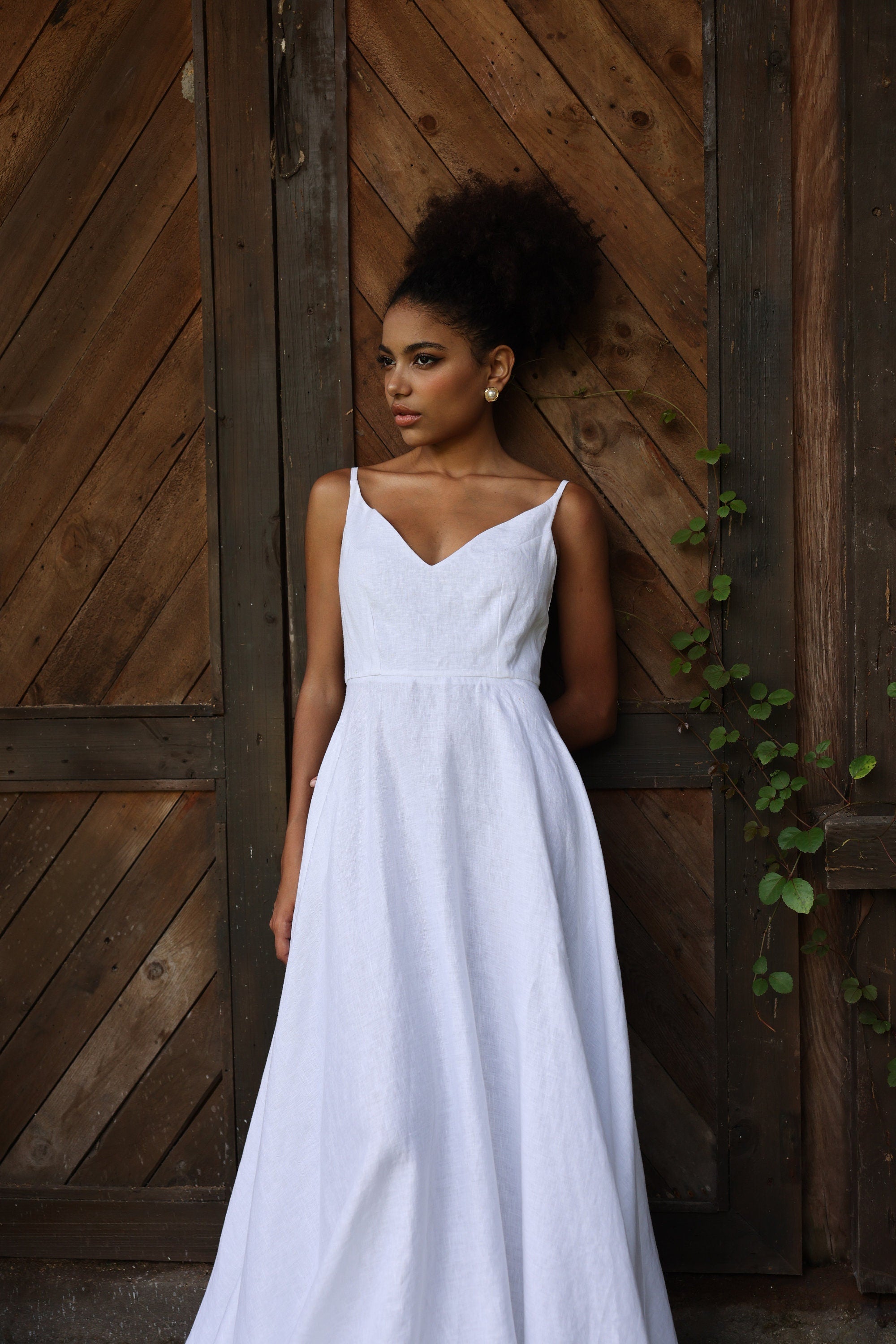 Woman in a white dress standing against a wooden wall with a rustic background