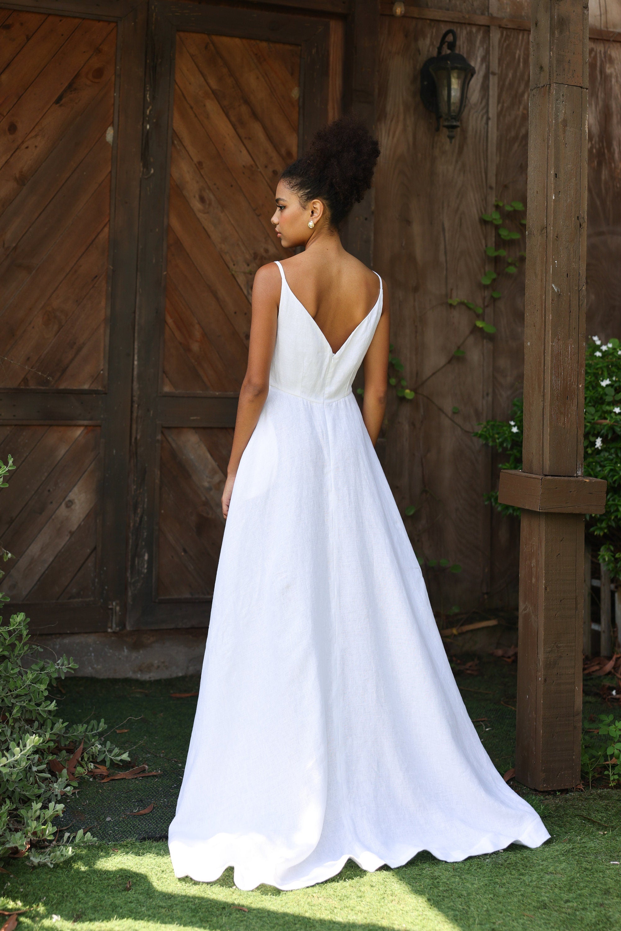 Woman in a white dress standing in front of wooden doors with greenery around.