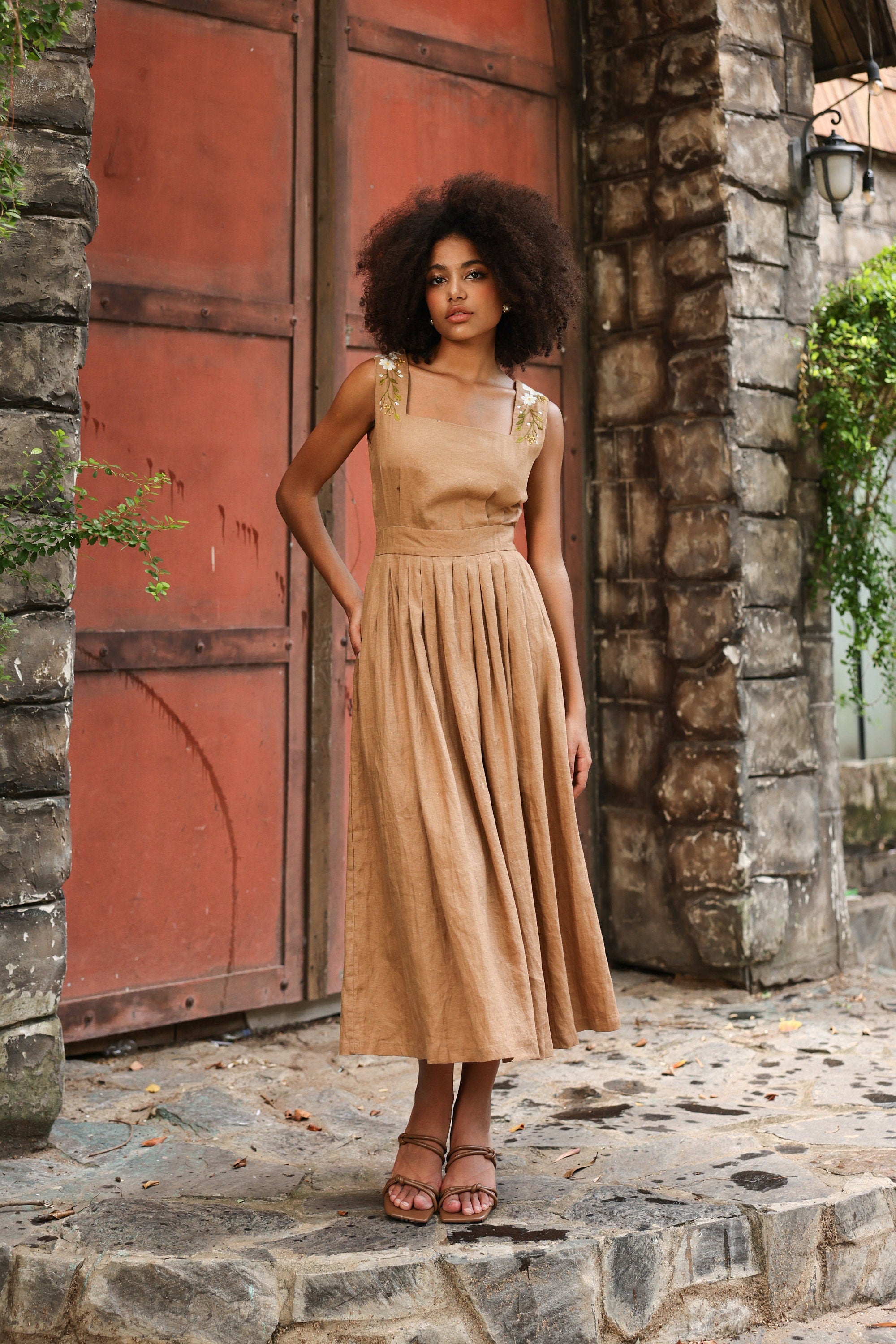 Woman in a dress standing in front of a stone wall with a red door.
