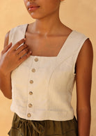 Woman wearing a beige sleeveless top with button details against a beige background