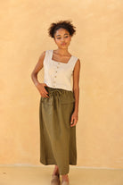 Woman wearing a sleeveless top with buttons and green skirt against a beige background