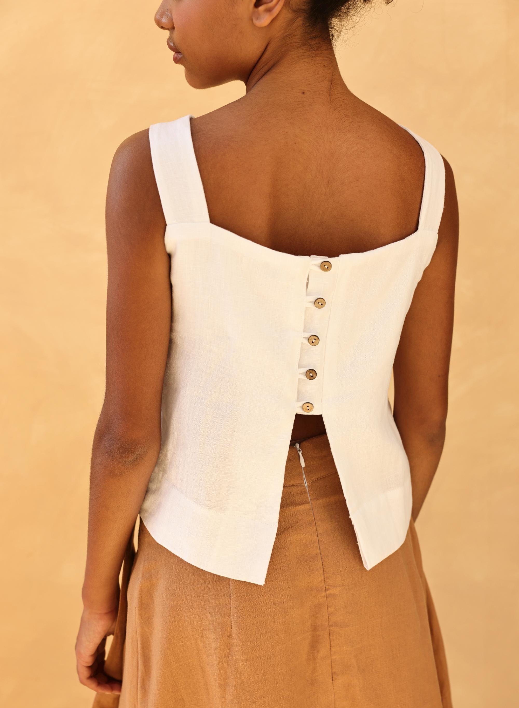 Person wearing a white sleeveless top with button details on a beige background