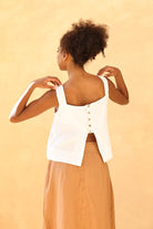 Woman wearing a white sleeveless top with buttons on a beige background