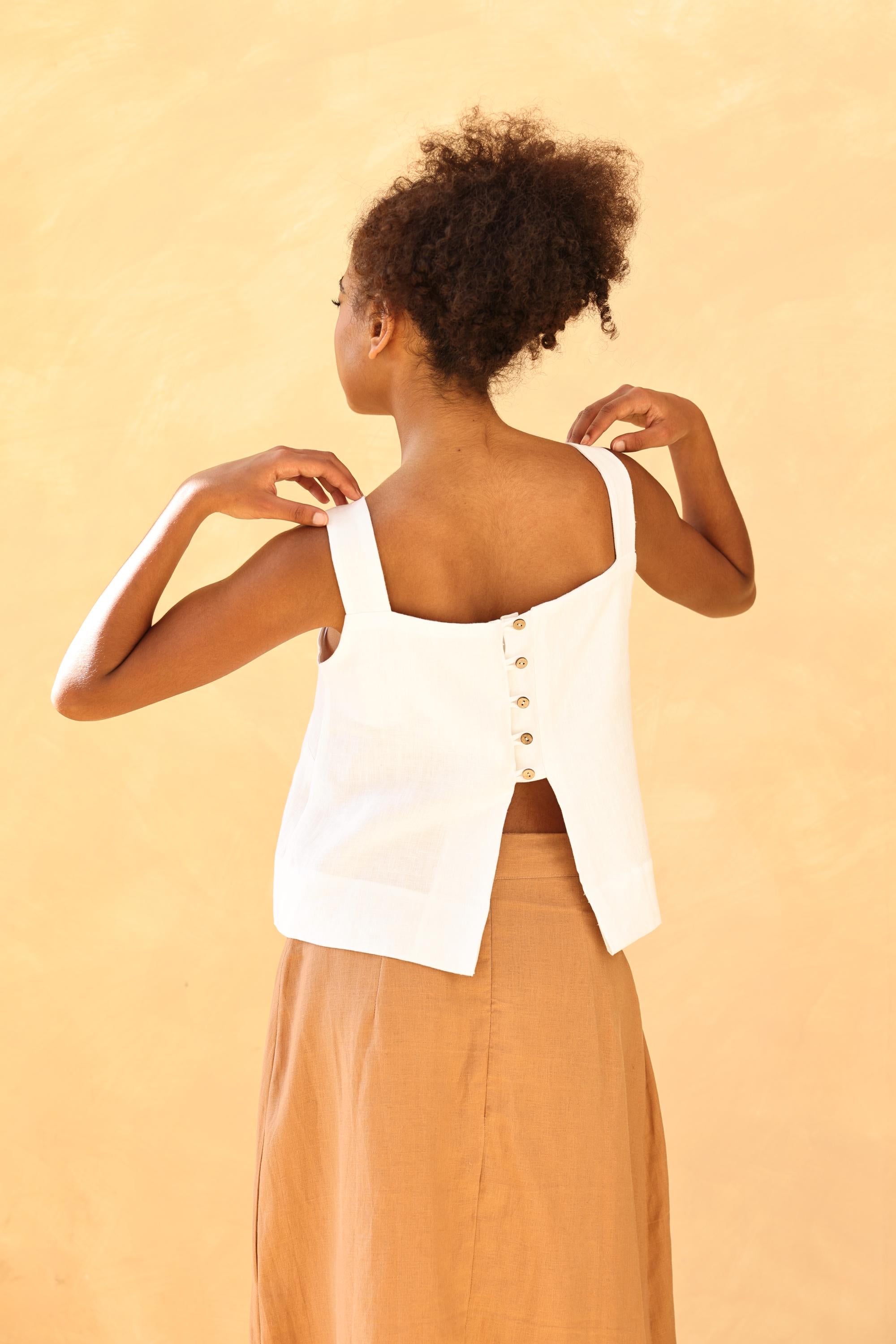 Woman wearing a white sleeveless top with buttons on a beige background