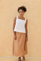 Woman wearing a white top and tan skirt against a beige background