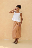 Woman wearing a white top and tan skirt against a beige background