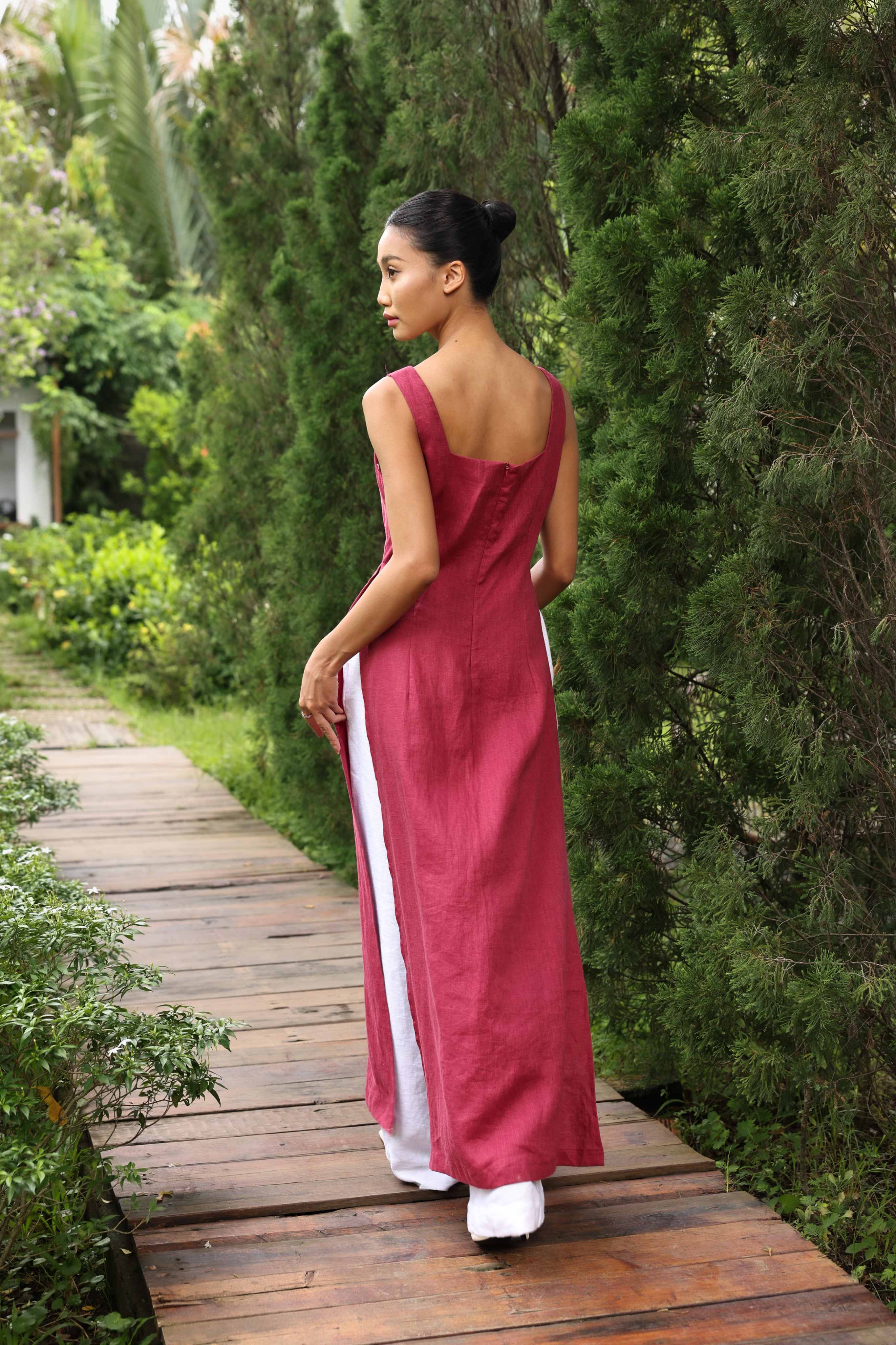 Woman in a red dress with white pants walking on a wooden path in a garden.