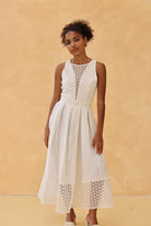 Woman wearing a white dress with lace details against a beige background