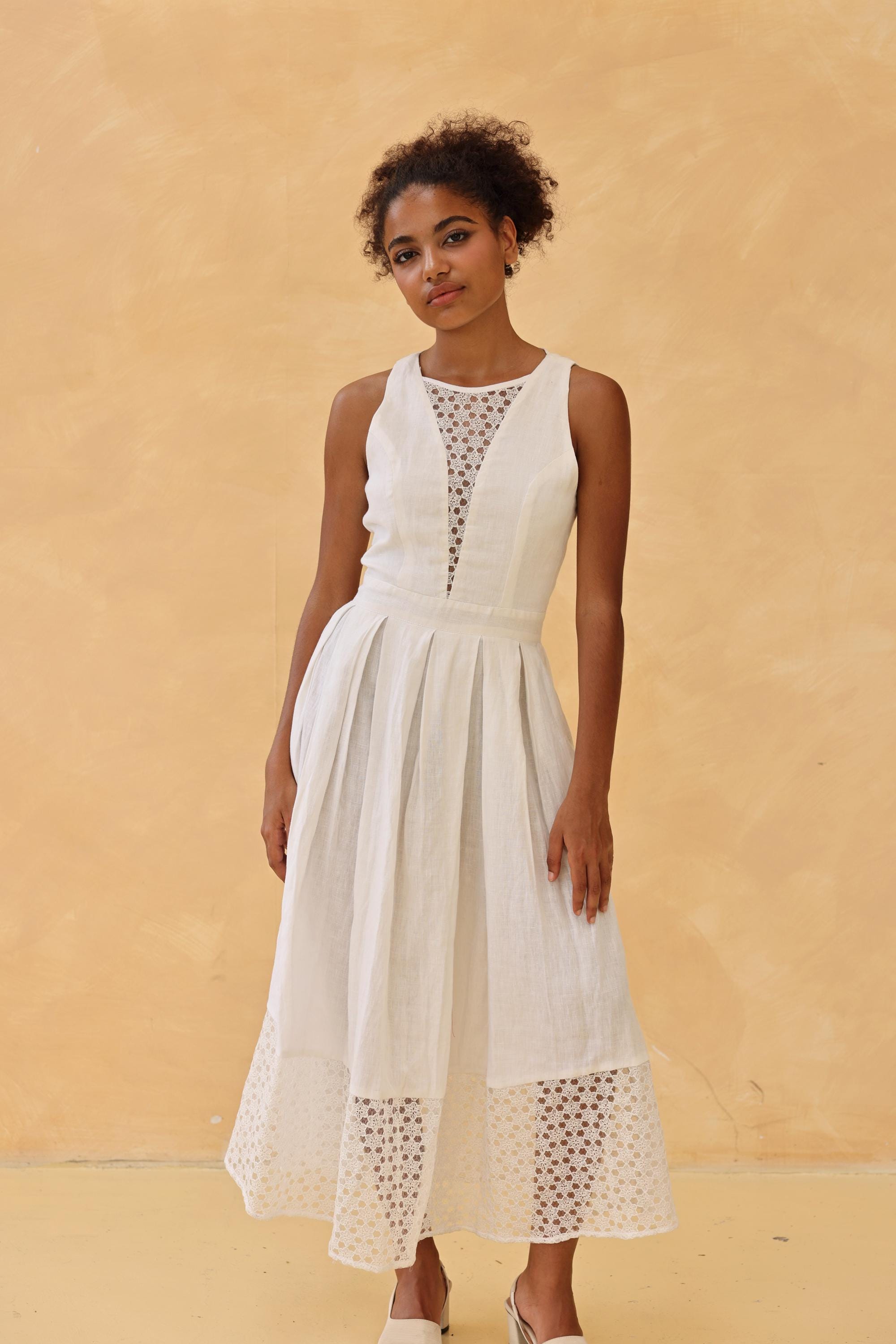Woman wearing a white dress with lace details against a beige background