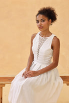 Woman in a white dress sitting on a wooden bench against a beige wall
