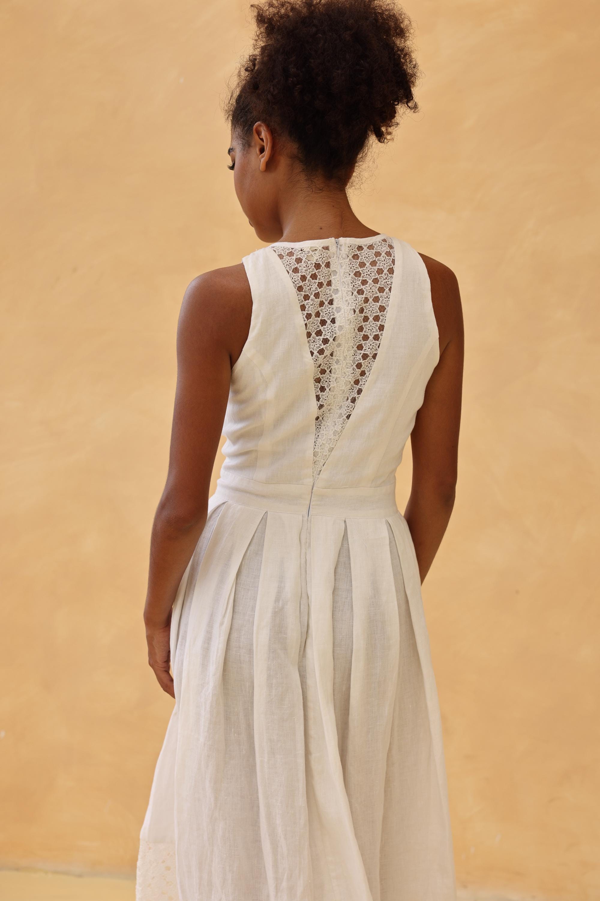 Woman wearing a white dress with intricate back design against a beige background