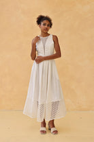 Woman wearing a white dress with lace details against a beige background