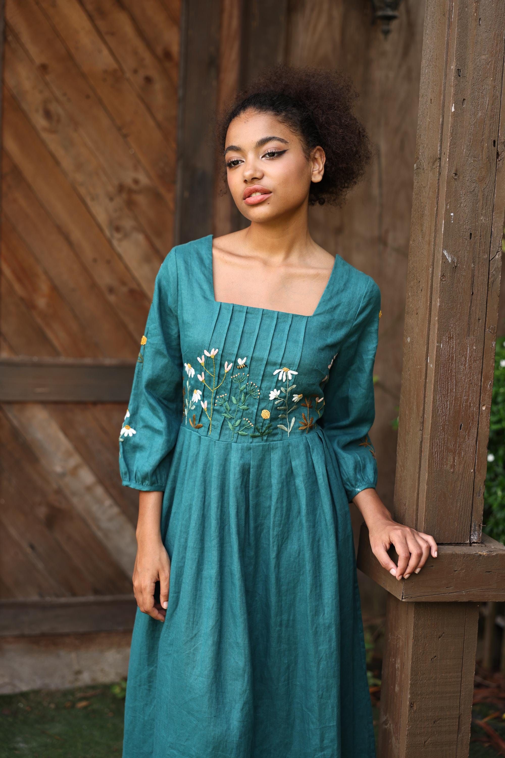 Woman wearing a teal dress with floral embroidery against a wooden background