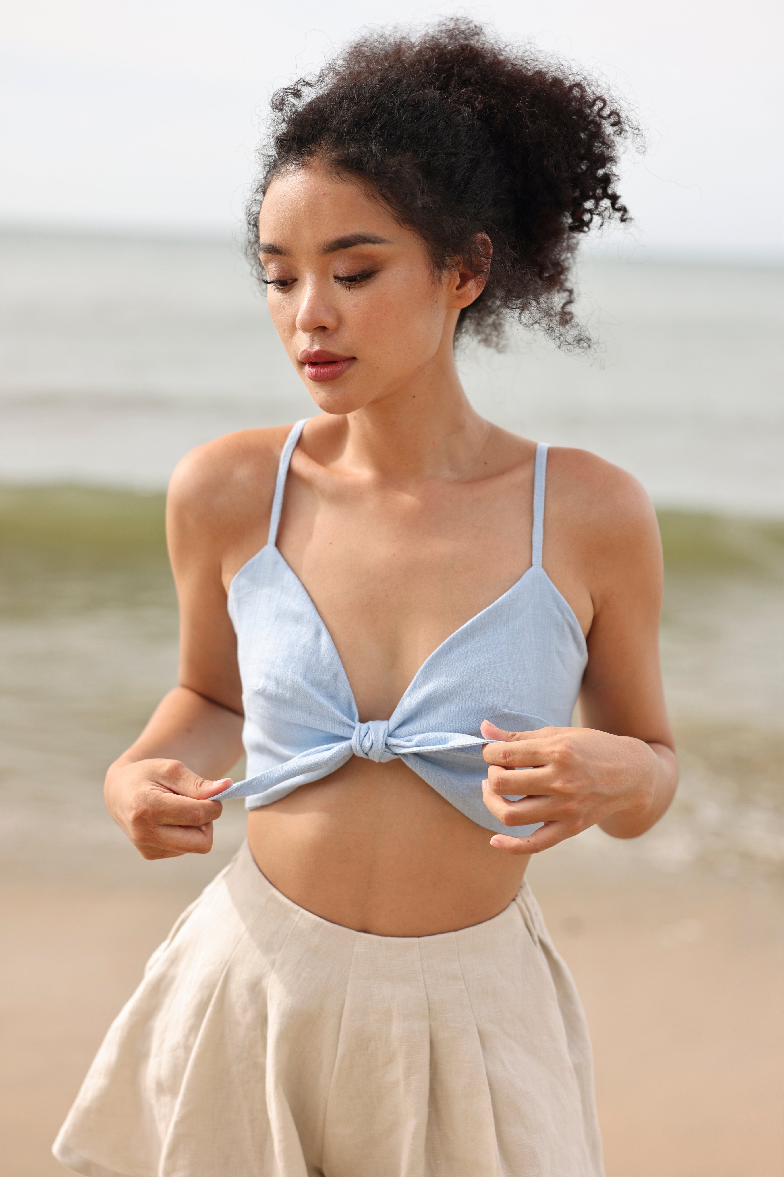 Woman wearing a light blue top and white shorts on a beach.