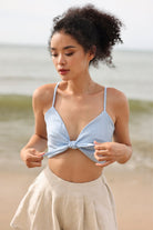 Woman wearing a light blue top and white shorts on a beach.