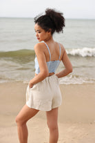 Woman standing on a beach wearing a light blue top and beige shorts.