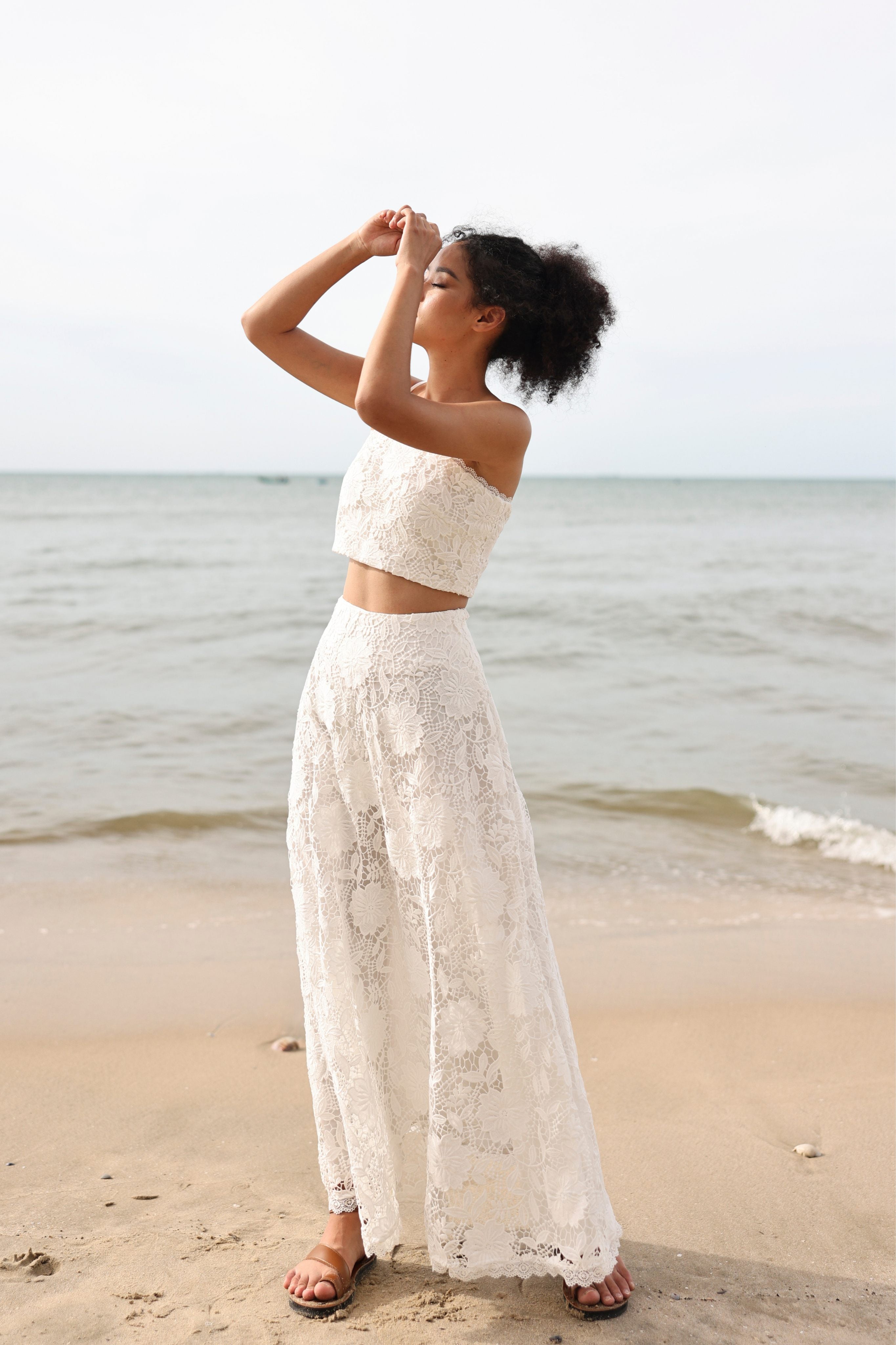 Woman in a white lace outfit standing on a beach with ocean in the background
