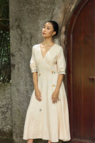 Woman in a dress standing against a textured wall and wooden door.