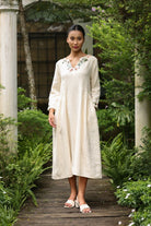 Woman in a dress standing on a wooden path in a garden.