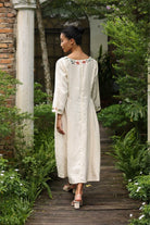 Woman in an embroidered dress walking through a garden.