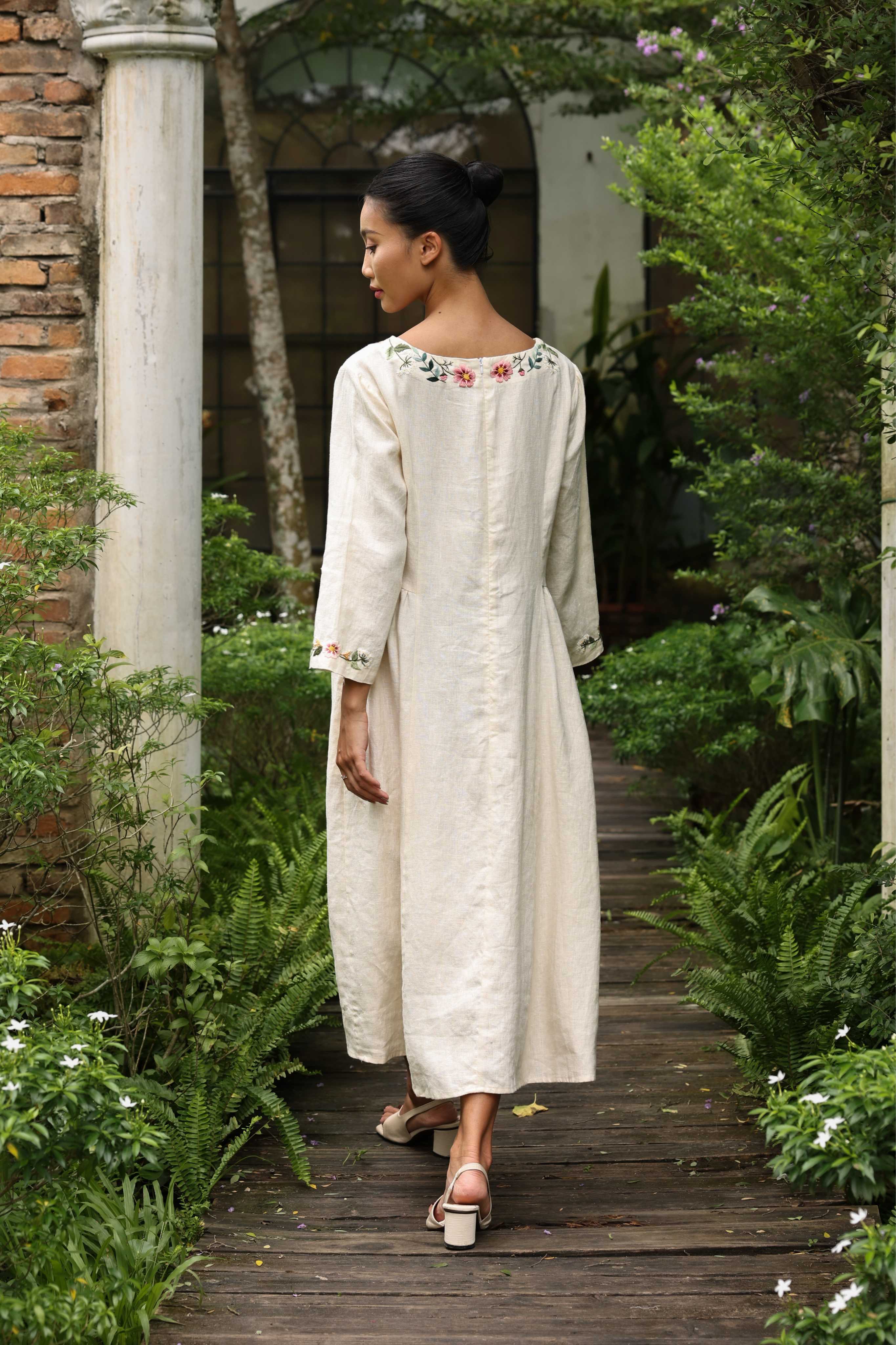Woman in an embroidered dress walking through a garden.