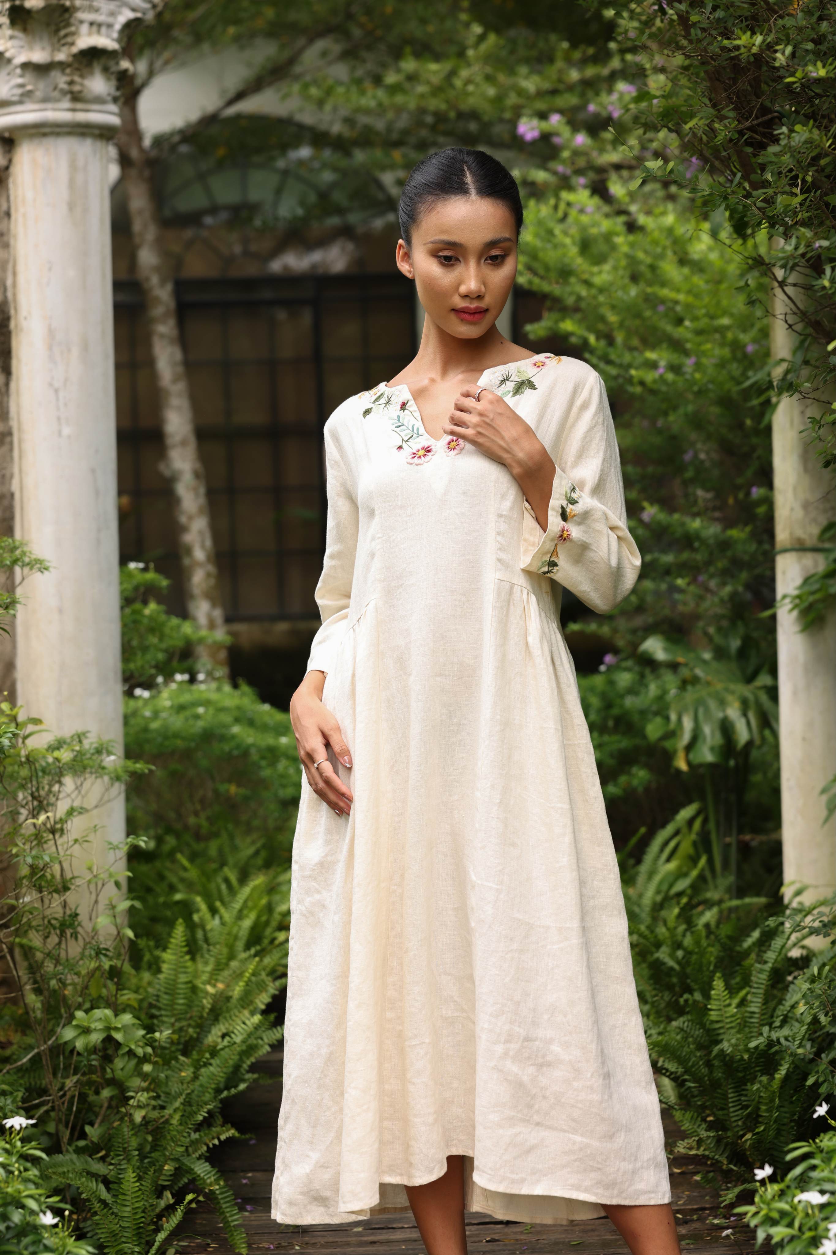 Woman in a dress standing in a garden with greenery and columns in the background