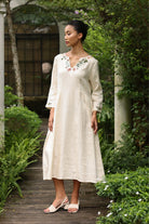 Woman in a dress with floral embroidery standing in a garden.