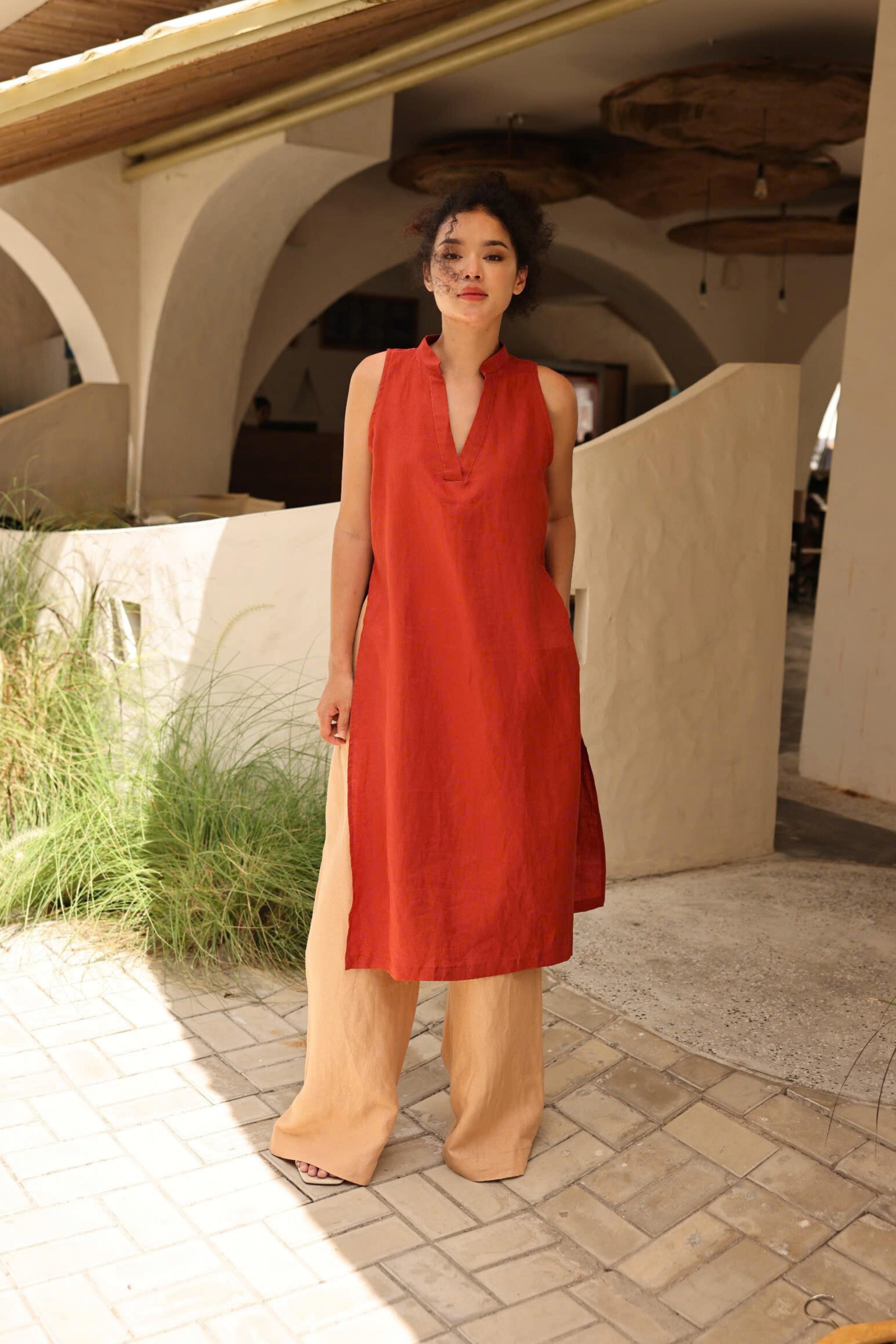 Woman in a red dress standing in an outdoor setting with arches and plants.